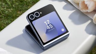 Galaxy Z Flip 6 in blue colorway on white table with grass next to white roses against a green grass background